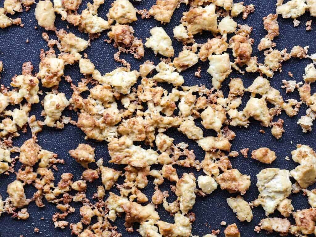 Golden brown scrambled eggs in small, uneven pieces spread across a black nonstick pan. The eggs appear slightly crispy in some areas, giving a textured look.